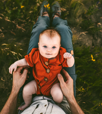 Ein Bild eines Babys in rotem Anzug, das auf dem Schoss des Vaters liegt und nach oben schaut